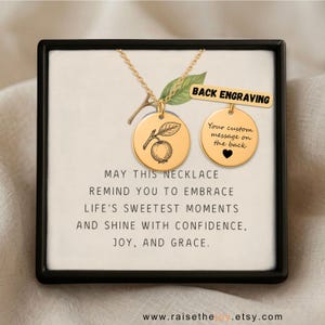 Op de afbeelding: Een goudkleurige ketting met een ronde hanger met een fruitillustratie. Een tweede ronde hanger toont de tekst BACK ENGRAVING, Your custom message on the back, en een hartje. De kaart vermeldt: MAY THIS NECKLACE REMIND YOU TO EMBRACE LIFE'S SWEETEST MOMENTS AND SHINE WITH CONFIDENCE, JOY, AND GRACE.