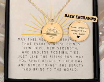 May include: A gold-toned circular pendant necklace featuring a sunrise engraving on the front and a blank space for custom text on the back. The pendant is displayed on a card with the text: MAY THIS NECKLACE REMIND YOU THAT EVERY SUNRISE BRINGS NEW HOPE, NEW STRENGTH, AND ENDLESS POSSIBILITIES. JUST LIKE THE RISING SUN, MAY YOU SHINE BRIGHTLY EACH DAY AND NEVER FORGET THE BEAUTY YOU BRING TO THE WORLD.