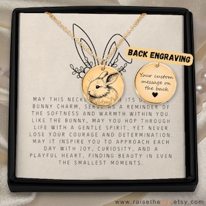 May include: A gold-coloured necklace with a circular pendant depicting a rabbit illustration. The necklace is displayed in a black box with text that says "Back Engraving" and "Your custom message on the back". The text below the necklace reads "May this necklace..."