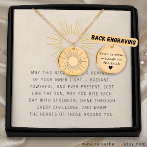 Op de afbeelding: Een goudkleurige ketting met een ronde hanger voorzien van een zonnestraalmotief. Een tweede ronde schijf toont de tekst BACK ENGRAVING en Your custom message on the back met een hartje. De ketting wordt gepresenteerd op een kaart met tekst.