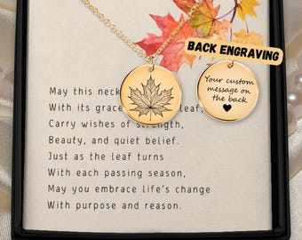 May include: Gold-colored necklace with a round pendant featuring a detailed maple leaf design. The necklace is presented in a black box with a card that has a poem about change. The back of the pendant is available for custom engraving.
