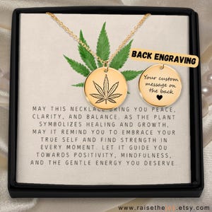 May include: A gold-coloured necklace with a circular pendant displaying a cannabis leaf design. The necklace is presented in a black box with text that reads "BACK ENGRAVING" and "Your custom message on the back". The background includes a cannabis leaf.