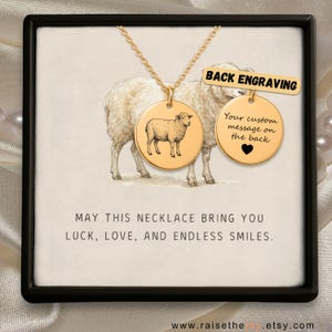 May include: A gold necklace with two circular pendants. One pendant has a detailed engraving of a sheep, and the other is for a custom message. The text "BACK ENGRAVING" is above the second pendant. The necklace is in a black box with the text "MAY THIS NECKLACE BRING YOU LUCK, LOVE, AND ENDLESS SMILES."
