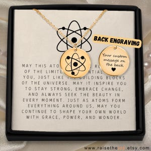 May include: Gold-colored atom pendant necklace with a black atom design. The necklace is displayed in a black box with a printed message. The text "Back Engraving" is visible, along with the Etsy website address.