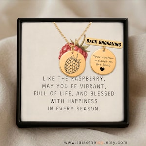 Op de afbeelding: Een goudkleurige ketting met ronde hanger, voorzien van een framboosgravure aan de voorzijde en ruimte voor een persoonlijke boodschap aan de achterzijde. De kaart bevat de tekst: Like the raspberry, may you be vibrant, full of life, and blessed with happiness in every season.
