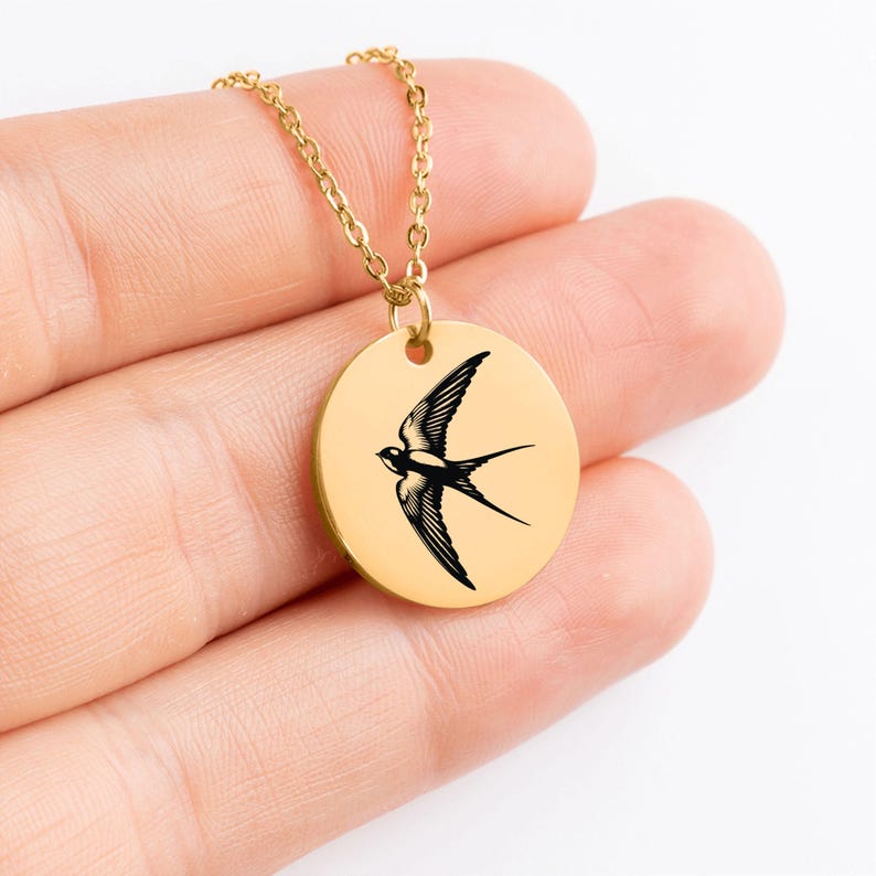 May include: Gold necklace with a round pendant featuring a black silhouette of a swallow in flight.