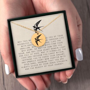 May include: A gold necklace with a pendant featuring a black and white silhouette of a bird. The pendant is in a box with a message that reads: "May this new boundless strength with grace swallow, may you find your way home, no matter how far you roam, and may your heart remain light and full of hope. May it symbolize the love and freedom you carry within, inspiring you to chase your dreams and embrace every new chapter with open arms, knowing that you are always guided by your inner strength and the beauty of your journey."