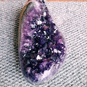 Può includere: Una grande geode di ametista viola con un gruppo di cristalli all'interno. La geode è liscia e lucida, e i cristalli sono affilati e appuntiti.