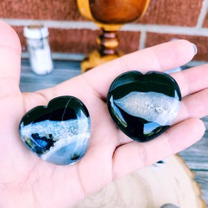 May include: Two black and white agate heart shaped stones. The stones have a white band across the centre and are polished.