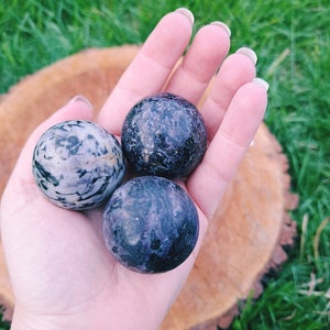 Puede incluir: Tres piedras lisas, redondas y pulidas en una mano. Las piedras son una mezcla de morado, negro y blanco.