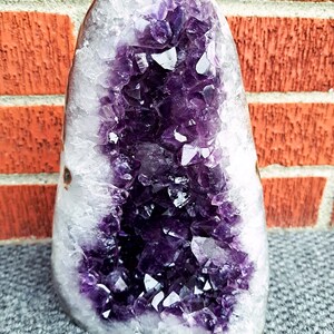Può includere: Una grande geode di ametista viola con un esterno naturale e ruvido e un interno liscio e lucido. La geode è piena di grappoli di cristalli viola scintillanti.