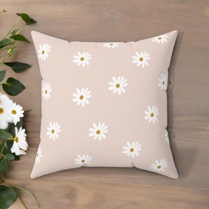 May include: A pink throw pillow with a white daisy pattern. The daisies have yellow centers.