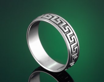 Peut inclure: Une bague en argent avec un motif de clé grecque. La bague est sur un fond vert.