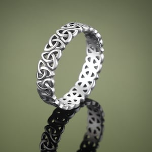 May include: A silver Celtic knot ring with a detailed design. The ring is on a green background.