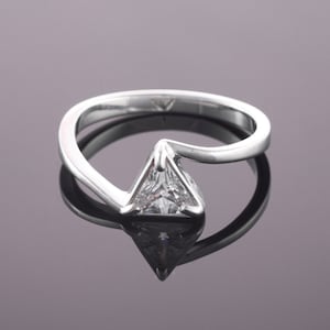 Peut inclure: Une bague en argent avec une pierre précieuse transparente de forme triangulaire sertie au centre. La bande de la bague est incurvée et présente un design moderne.