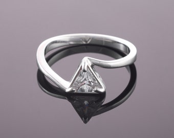 May include: A silver ring with a triangular shaped clear gemstone set in the center. The band of the ring is curved and has a modern design.
