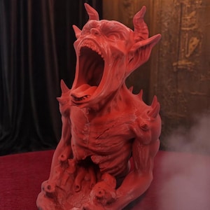 May include: A red, demonic sculpture with a wide open mouth and sharp teeth. The sculpture is made of a textured material and has a detailed design.