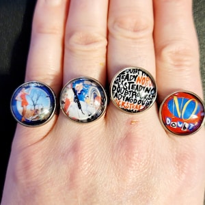 May include: Four silver-toned rings with circular designs. One ring features a woman in a red dress, another has a band image, a third ring has the words "NO DOUBT" and the last ring has the words "READY NO DOUBT" in a circular pattern.