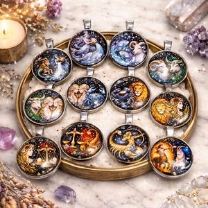 May include: A collection of round pendants featuring zodiac cusp designs. Each pendant has a silver-colored bail and showcases colorful illustrations of astrological symbols and celestial backgrounds. The words "Zodiac Cusp Pendants" are at the top.