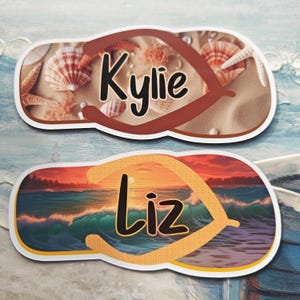 May include: Two flip-flop shaped name tags. One shows a beach scene with seashells and the name "Kylie" in black script. The other depicts a sunset over the ocean with the name "Liz" in black script.