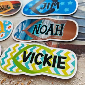 May include: Close-up of several personalized flip-flop stickers. The stickers feature names like "Jim," "Noah," and "Vickie" in bold black font. Designs include blue with stars, a beach scene, and a yellow and green zigzag pattern.