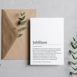 May include: A white card with the word "Jubil&auml;um" in black text. The card defines the word "Jubil&auml;um" in German, explaining that it is a special moment that celebrates milestones and shared experiences. The card is on a gray background with green foliage.