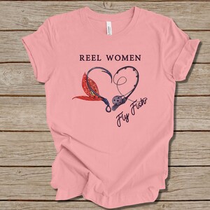 May include: Pink t-shirt with the text "Reel Women Fly Fish" and a graphic of two fishing hooks forming a heart shape with a fly on one hook.