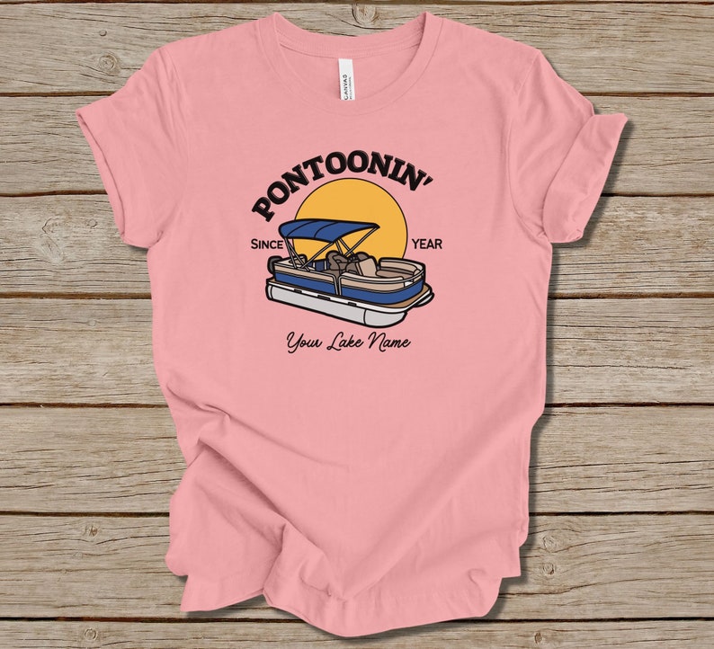 K&ouml;nnte beinhalten: Rosa T-Shirt mit einem Grafikdruck eines Pontonboots auf einem See mit einer Sonne und dem Text "Pontoonin' Since Year" und "Your Lake Name".