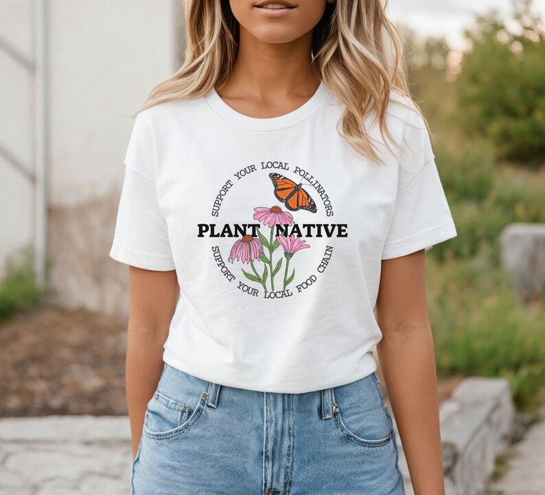 Pode incluir: Camiseta branca com um design gr&aacute;fico circular que apresenta uma borboleta, flores e o texto "Apoie seus polinizadores locais Plante nativos Apoie sua cadeia alimentar local".