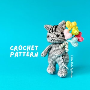 May include: A grey crocheted cat holding a bunch of colourful heart-shaped balloons. The cat has black stripes and a white face. The text "CROCHET PATTERN" is in the top left corner of the image. The text "Little Pixie By Marie" is in the bottom right corner of the image.