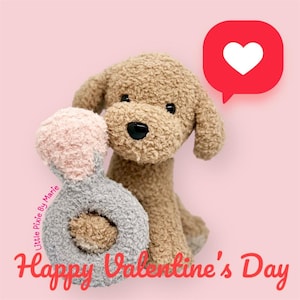 May include: A brown plush dog toy holding a pink and gray ring toy. The dog is sitting on a pink background with a red speech bubble with a white heart in it. The text "Happy Valentine's Day" is written in red below the dog.
