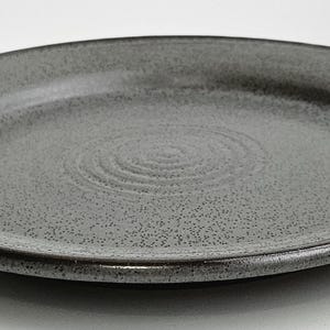 May include: A speckled gray ceramic plate with a dark brown rim. The plate has a slightly raised edge and a textured surface. The center of the plate features a spiral design. This plate is suitable for serving food.