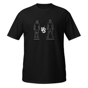May include: Black t-shirt featuring a white graphic of two soccer players facing each other, with "VS" in between. The names "Lionel Messi" and "Cristiano Ronaldo" are printed below the figures. The shirt is made of a soft material.