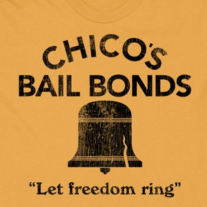 May include: A yellow t-shirt with black text that reads "Chico's Bail Bonds" and a black silhouette of the Liberty Bell with the text "Let freedom ring".