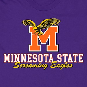 Może przedstawiać: Fioletowy T-shirt z pomarańczową literą "M" i lecącym nad nią żółtym orłem. Pod literą "M" znajduje się napis "MINNESOTA STATE Screaming Eagles".