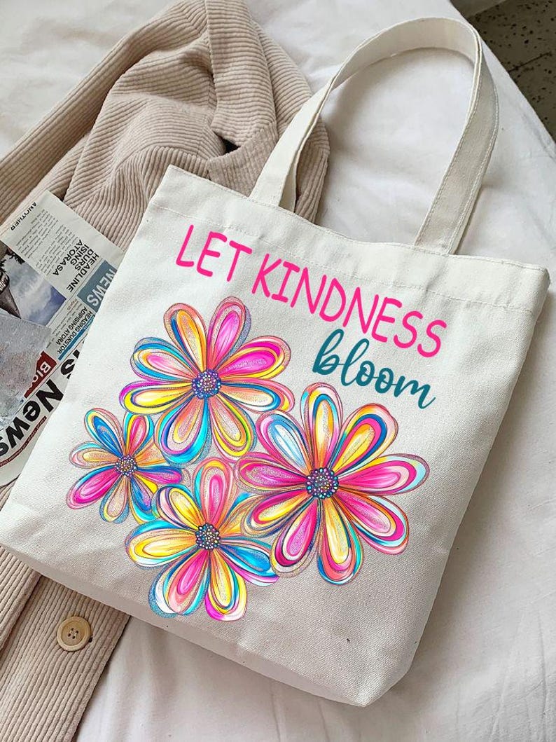 K&ouml;nnte beinhalten: Wei&szlig;e Stofftasche mit bunten Blumen und dem Text "LET KINDNESS bloom".