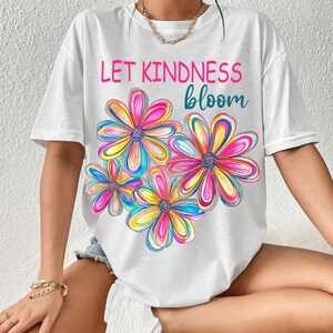 K&ouml;nnte beinhalten: Wei&szlig;es T-Shirt mit einem grafischen Druck von bunten Blumen und dem Text "Let Kindness Bloom".