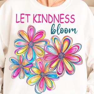 Puede incluir: Sudadera blanca con el texto "Let Kindness Bloom" en letras rosa y azul. El texto está rodeado de cuatro flores coloridas con pétalos rosas, amarillos, azules y blancos.