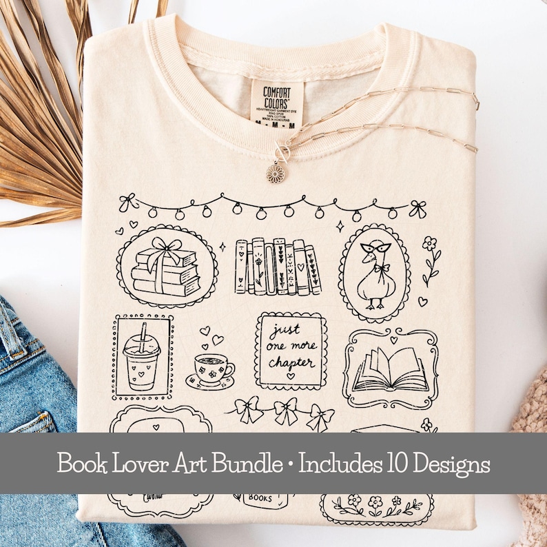 May include: A cream-colored t-shirt featuring a black line art graphic of books, a goose wearing glasses, a coffee cup, a drink, and the text "just one more chapter" inside decorative frames, with a string of lights and bows above the designs.