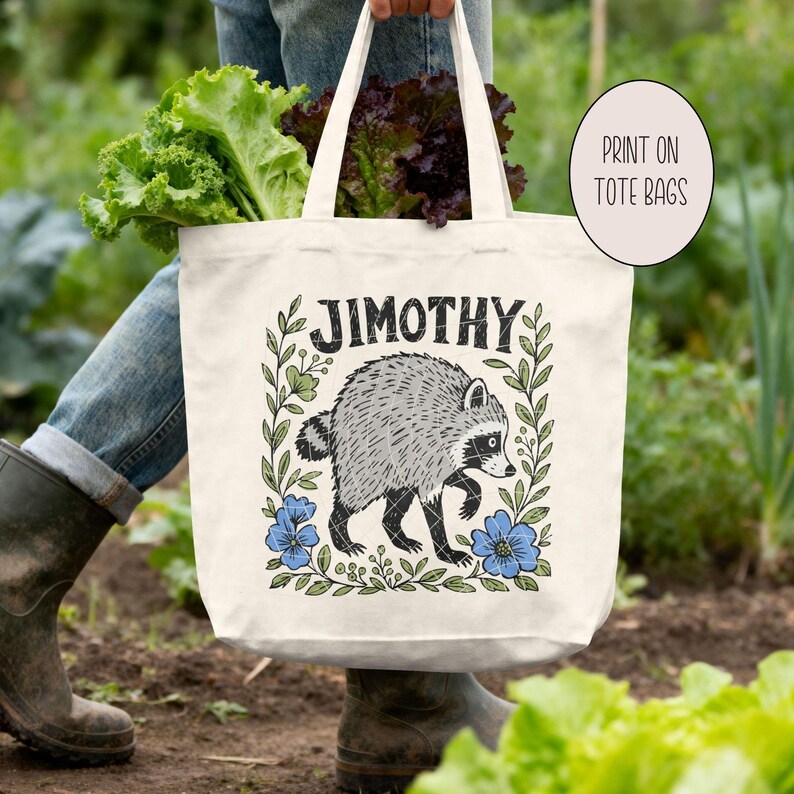 May include: A cream-colored canvas tote bag featuring a black and white illustration of a raccoon surrounded by a floral wreath and the text JIMOTHY. The design includes blue flowers and green leaves, with the text PRINT ON TOTE BAGS in a circle.