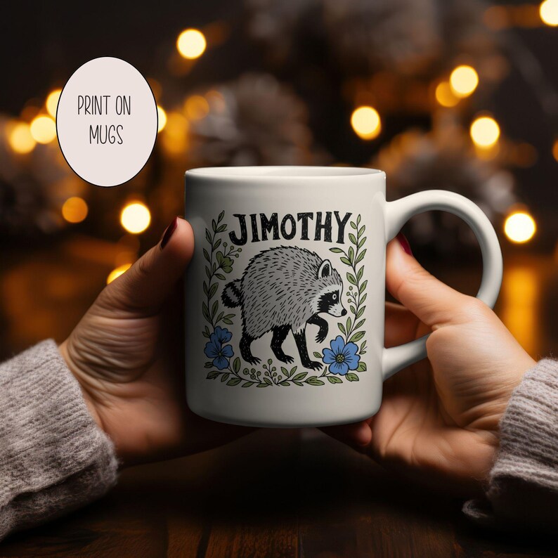 May include: A white ceramic mug featuring a black and white illustration of a raccoon surrounded by green leaves and blue flowers. The name JIMOTHY is printed in black capital letters above the raccoon. The mug has a curved handle on the right side.