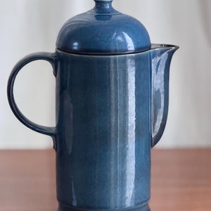May include: A blue ceramic teapot with a lid and a handle. The teapot has a glossy finish and a slightly rounded shape.