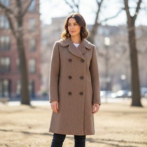 May include: A brown double-breasted coat with a textured pattern. The coat features a rounded collar and six dark buttons. The coat is knee-length and worn over a white top and black pants. The background shows trees and buildings.