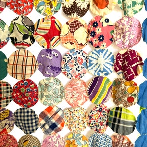 Könnte beinhalten: Eine Patchwork-Decke mit einem kreisförmigen Muster. Die Decke besteht aus verschiedenen Stoffen mit Blumen-, geometrischen und karierten Mustern in Rot-, Blau-, Grün-, Lila- und Weißtönen.