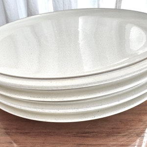 May include: Three white ceramic plates stacked on top of each other. The plates are oval shaped and have a slightly raised rim.