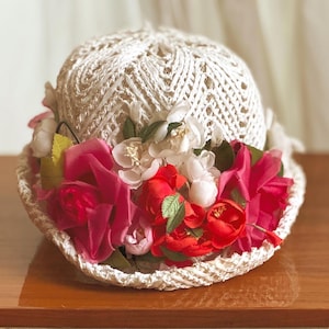 May include: A white crocheted hat with pink and red fabric flowers.