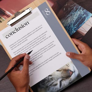 May include: A close-up of a clipboard with a white sheet of paper on it. The paper has the word "conclusion" written in bold black letters at the top. The text below discusses the responsibilities of pet ownership. A hand is holding a black pen and writing on the paper. The clipboard is on a wooden surface. A cat's face is visible in the bottom right corner of the image.