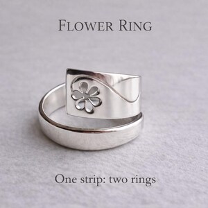 Op de afbeelding: Een zilveren ring met een bloemmotief. De ring heeft een rechthoekige bovenkant met een uitgesneden bloem en een gebogen band. De tekst "FLOWER RING" en "One strip: two rings" zijn zichtbaar.