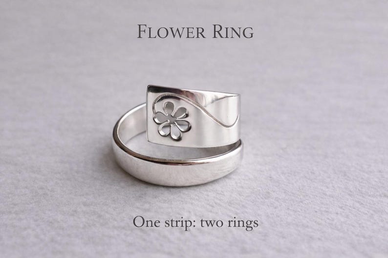Op de afbeelding: Een zilveren ring met een bloemmotief. De ring heeft een rechthoekige bovenkant met een uitgesneden bloem en een gebogen band. De tekst "FLOWER RING" en "One strip: two rings" zijn zichtbaar.