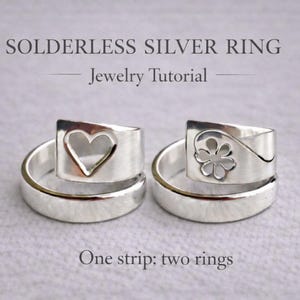 Op de afbeelding: Twee zilveren ringen met unieke ontwerpen. E&eacute;n ring heeft een hartvormige uitsparing, de andere een bloem. De ringen maken deel uit van een sieraden tutorial, zoals aangegeven door de tekst "Solderless Silver Ring - Jewelry Tutorial". Gemaakt van &eacute;&eacute;n strip.